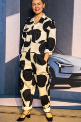 A person wearing a black and white dotted boiler suit standing in front of a Volvo car backdrop.