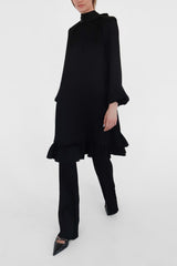 Person wearing a black dress and pants on a white background